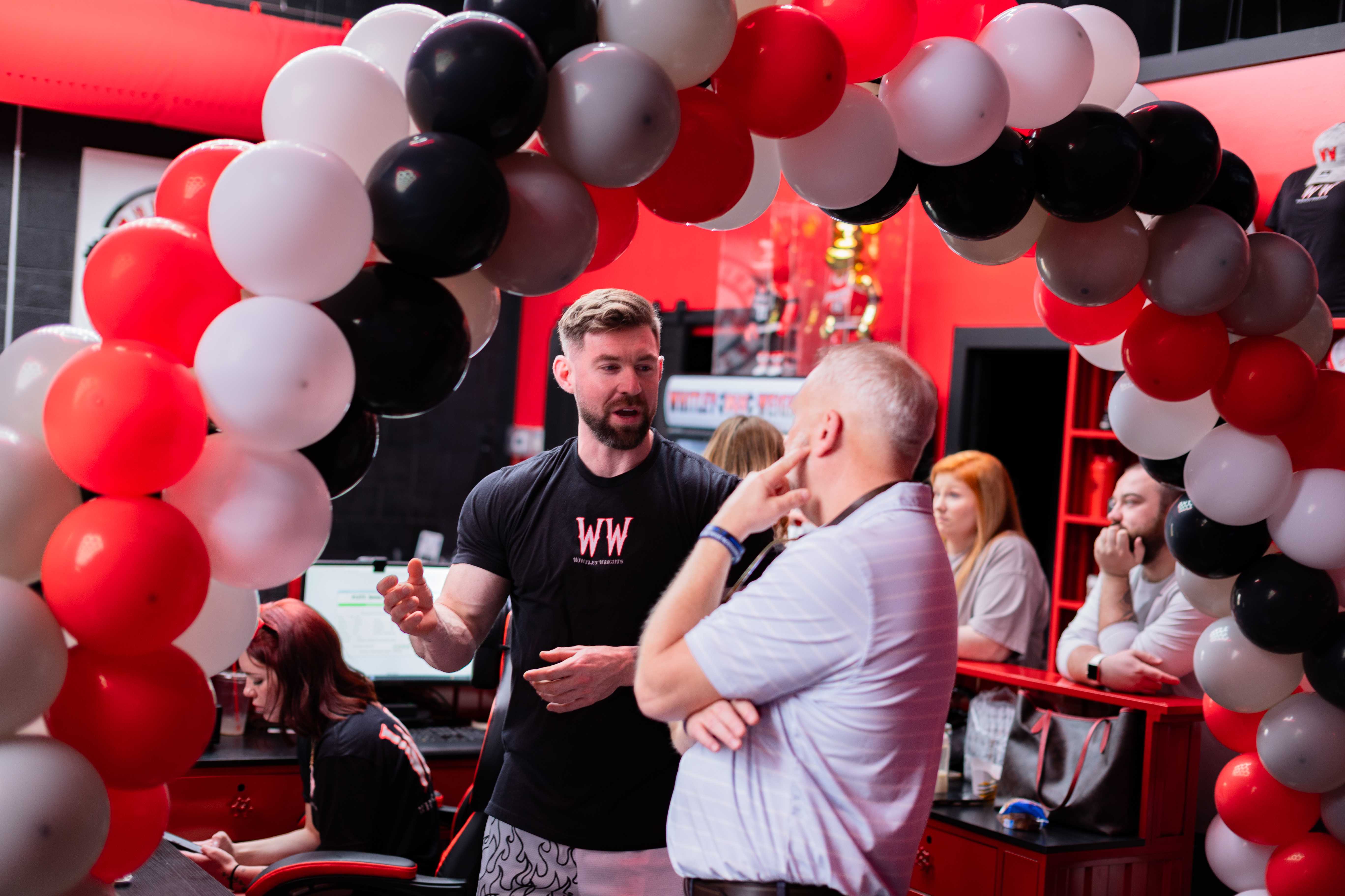 Owner talking with a member under the balloon arch at the grand opening