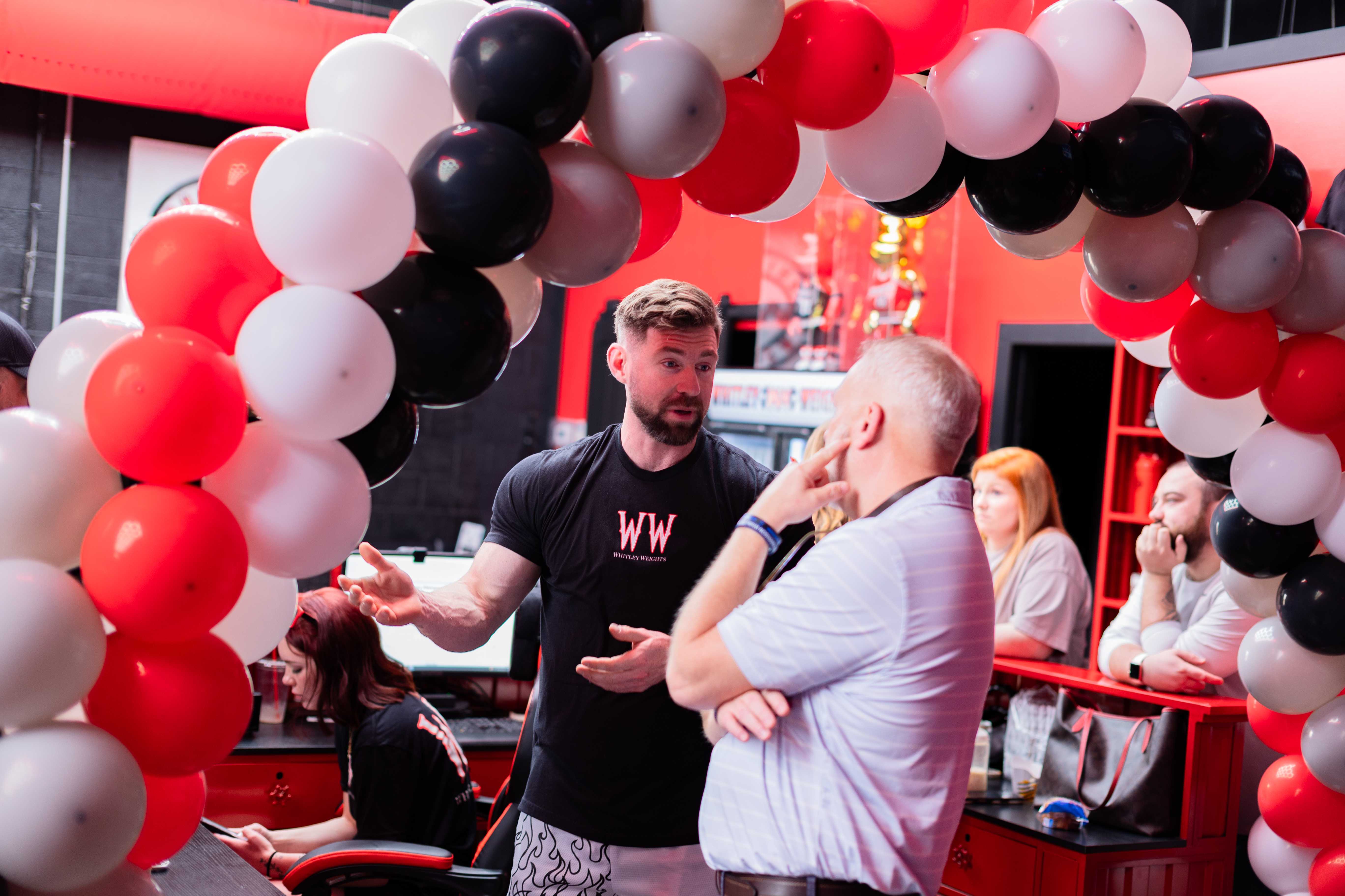 Grand opening conversation beneath the red and black balloon arch