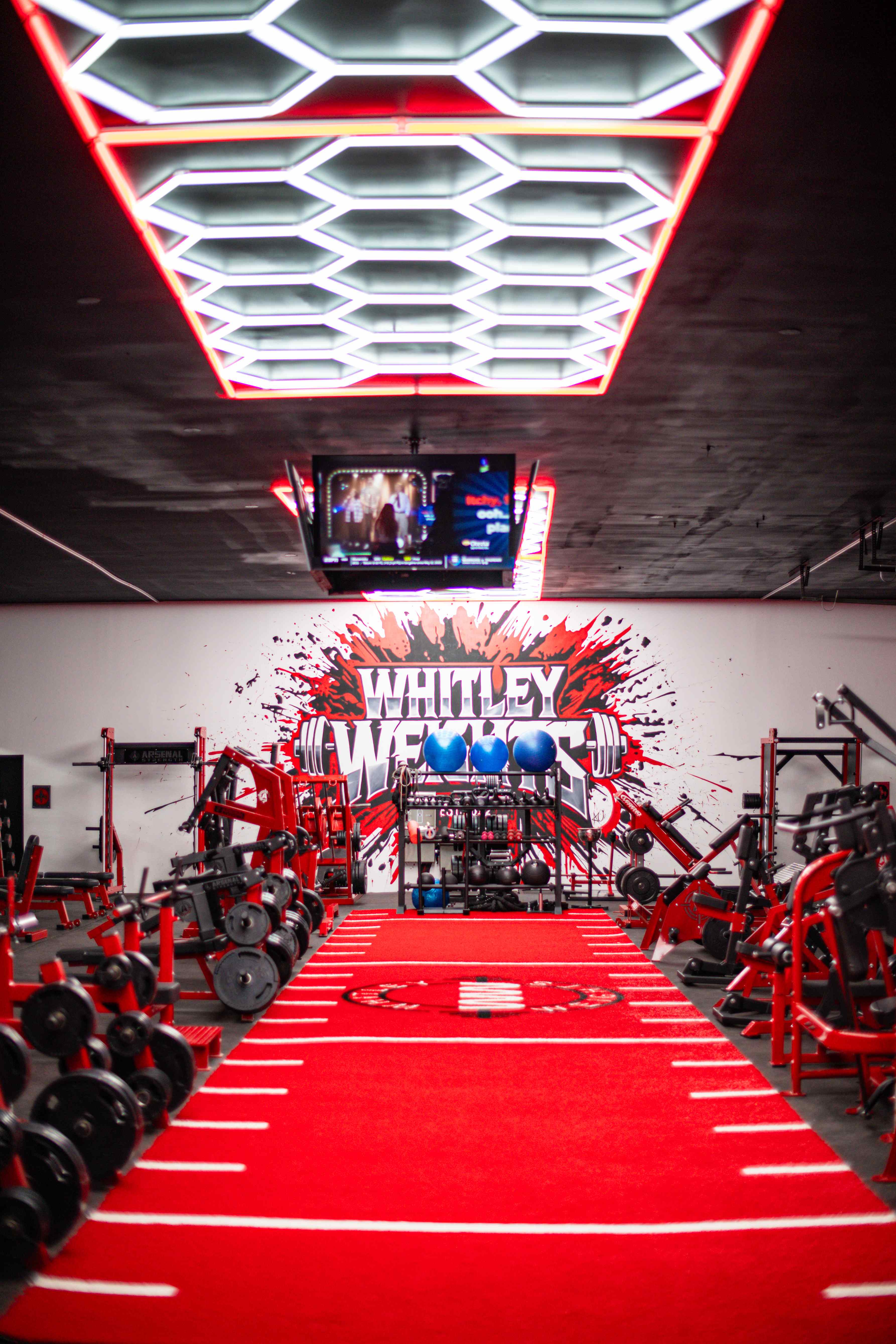 Red turf runway leading to the Whitley Weights mural under hex lighting
